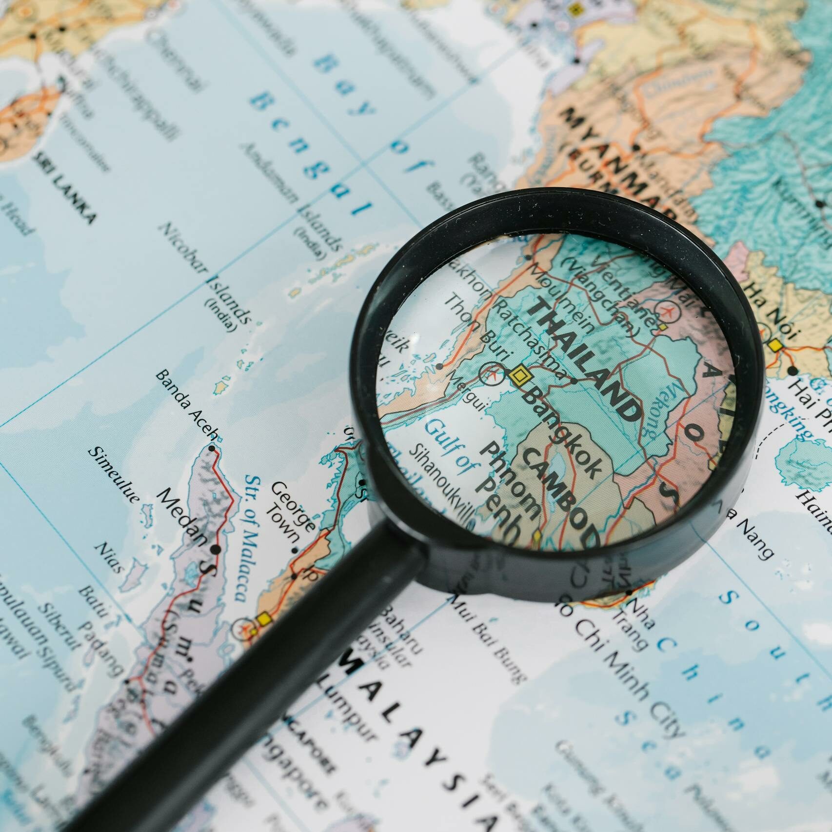 A magnifying glass highlighting Thailand on a detailed world map, ideal for travel-themed visuals.